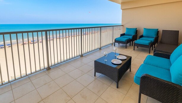 A balcony with a view of the beach, wicker furniture, and a table with plates and glasses. - Sweeping 5th Floor Views - Direct Beach - Remodeled (South Padre Island)