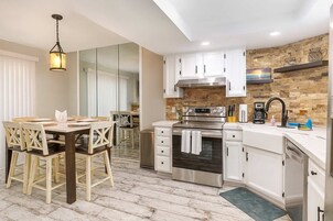 A modern kitchen with white cabinets, stainless steel appliances, and a brick accent wall.