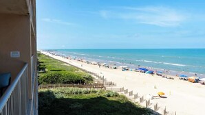 A beach with umbrellas and people, a pier in the distance, and a clear sky. - Sweeping 5th Floor Views - Direct Beach - Remodeled (South Padre Island)