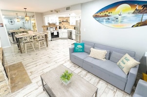 A modern living room with a grey sofa, a coffee table with a plant, and a dining area with wooden furniture.