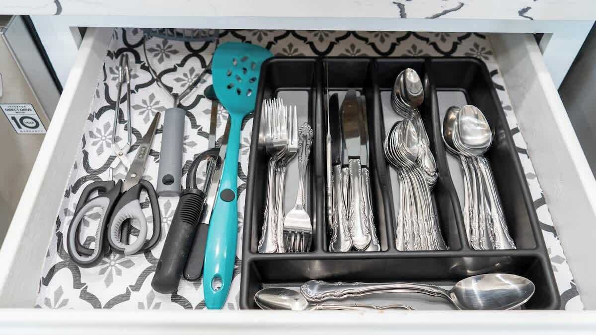 Eine Schublade mit ordentlich angeordneten Küchenutensilien, darunter ein türkisfarbener Pfannenwender, verschiedene Gabeln, Messer und Löffel.