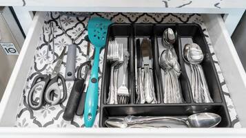 A drawer with neatly organized kitchen utensils including a turquoise spatula, various forks, knives, and spoons.
