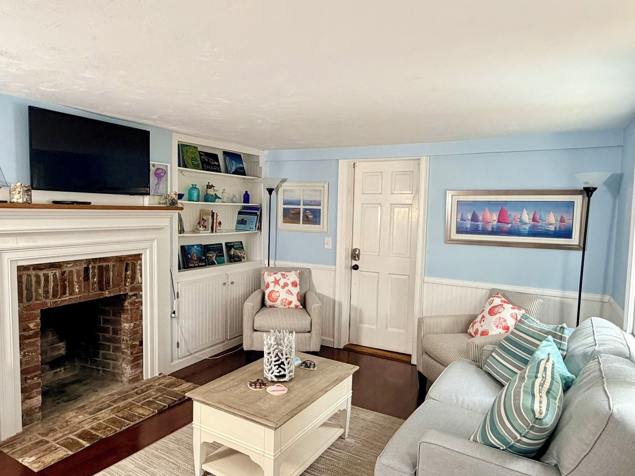 Ein Wohnzimmer mit Kamin, Fernseher, Bücherregal, Sofa und einem Gemälde an der Wand.