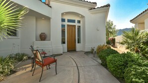 Una casa con fachada blanca, puerta de madera y un patio con sillas.