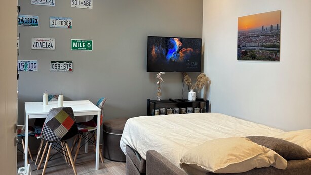 A modern bedroom with a skylight, a bed, a desk, a TV, and a cityscape painting.