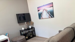 A living room with a sofa, a TV mounted on the wall, a console table with decorative items, and a painting of a pier.
