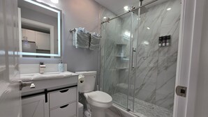 Et moderne badeværelse med en glasvæg omkring brusenichen, toilet og et vaskeskab med skuffer.