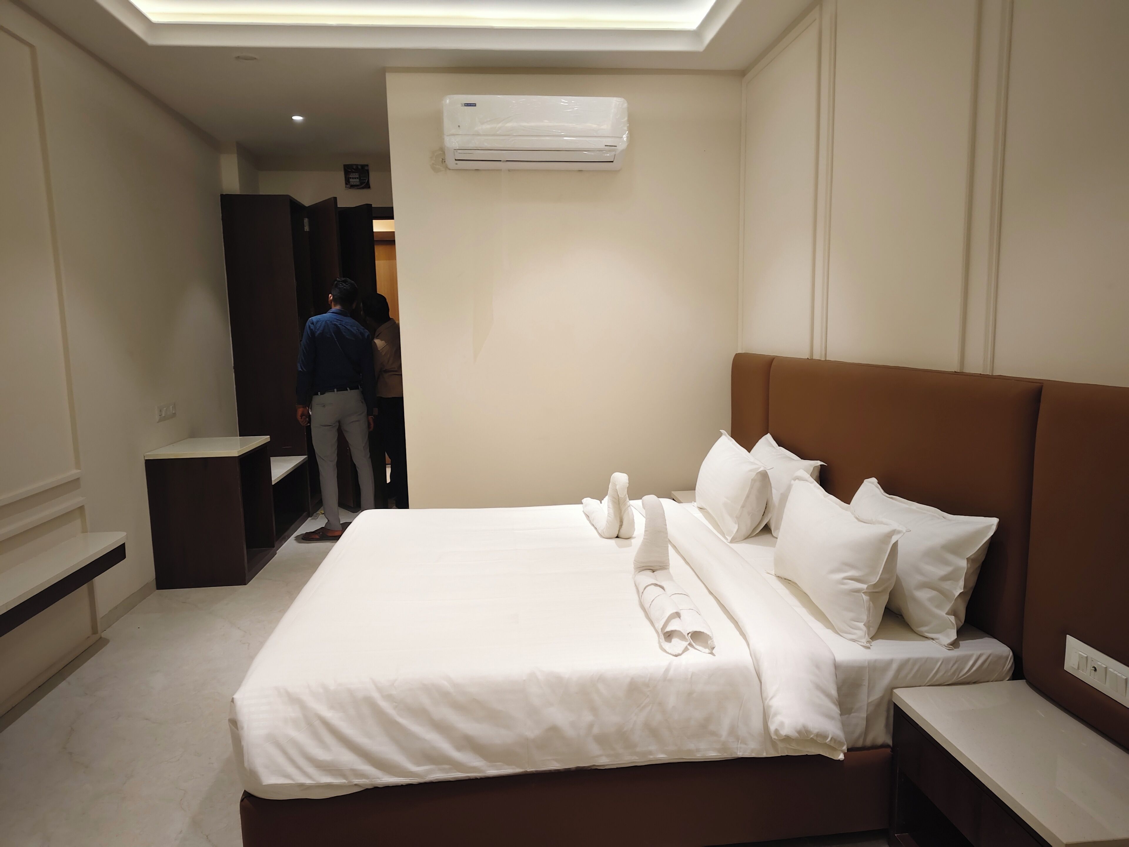 Una camera d'albergo con un letto rifatto, un comodino e un condizionatore d'aria montato a parete.