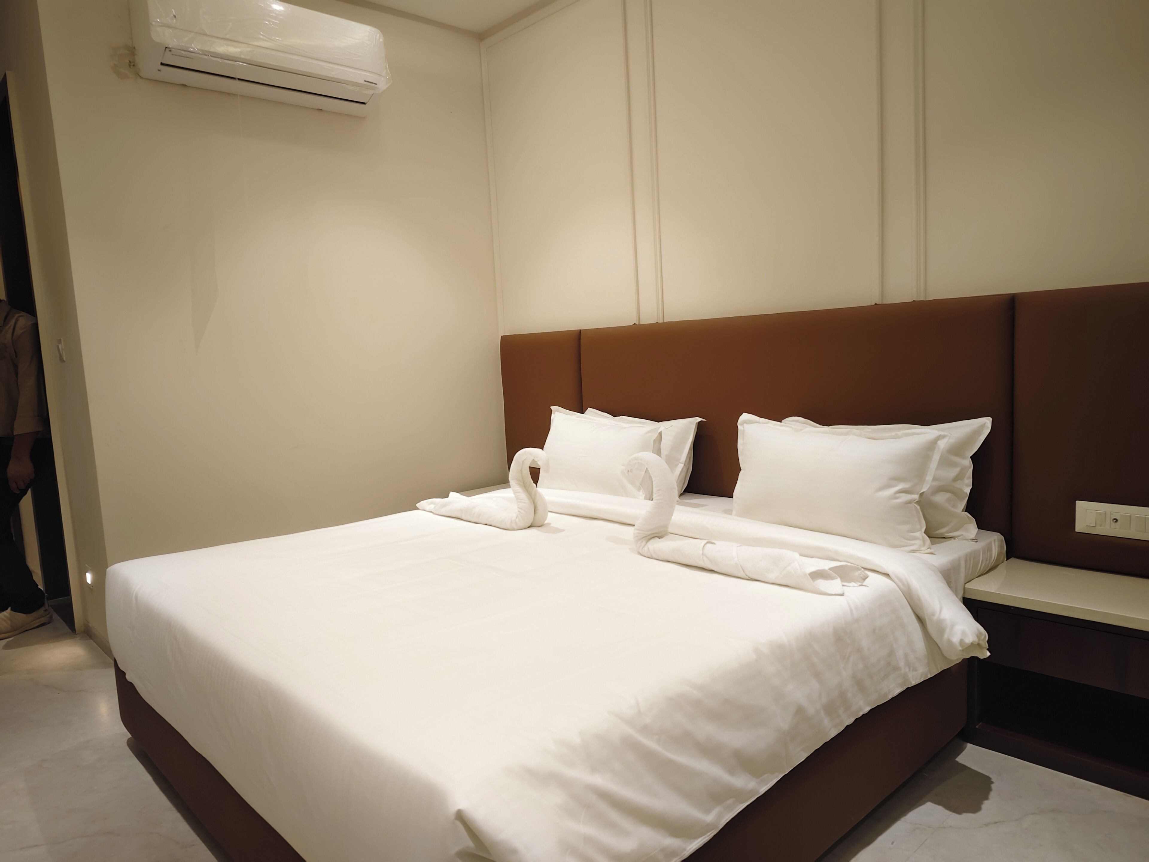 A hotel room with a bed, a brown headboard, white pillows, and a swan-shaped towel arrangement.
