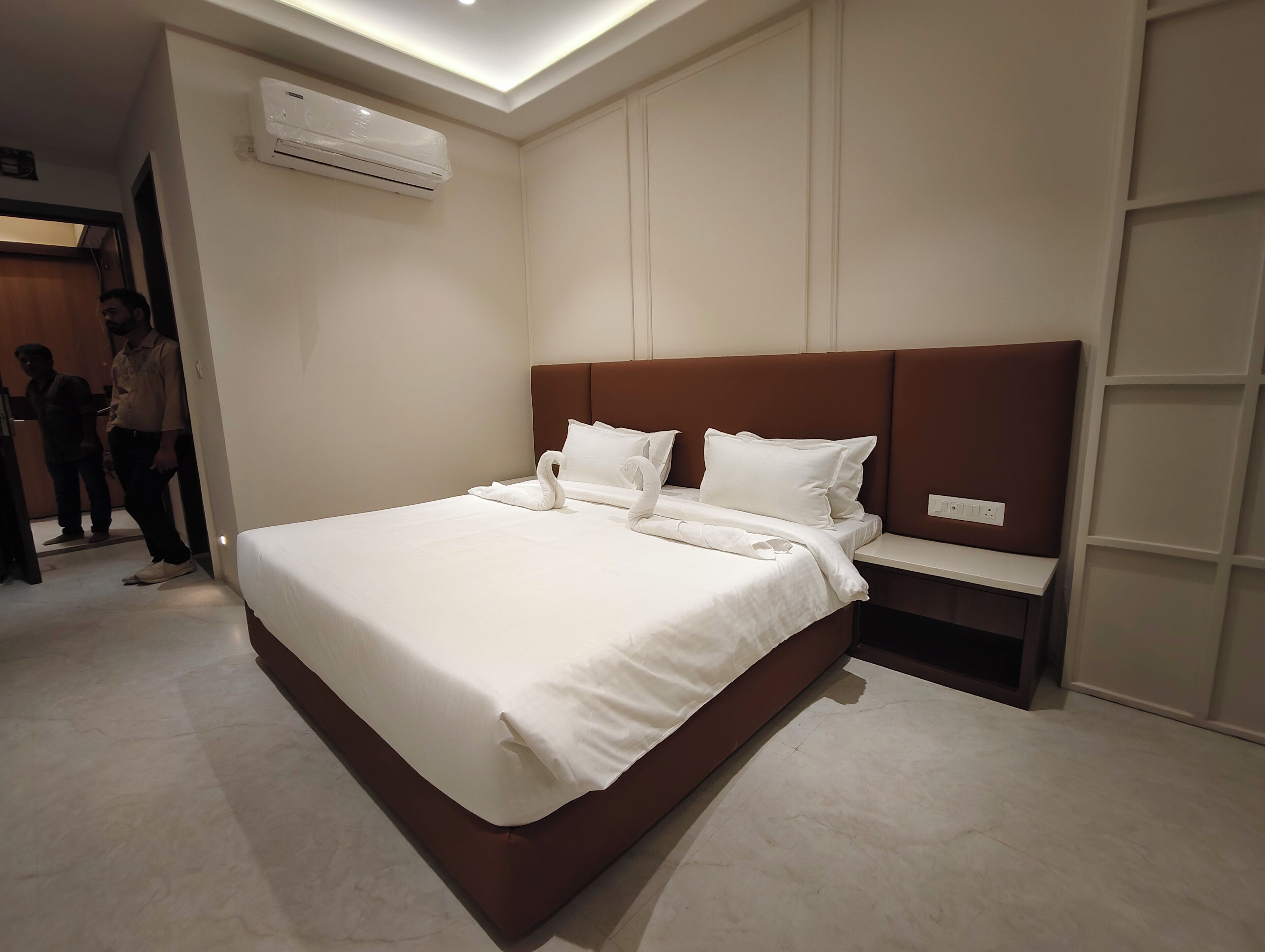 A modern hotel room with a large bed, a built-in nightstand, and an air conditioning unit on the wall.