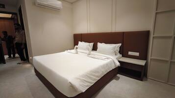 A modern hotel room with a large bed, a built-in nightstand, and an air conditioning unit on the wall.
