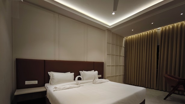 A modern hotel room with a large bed, a nightstand, a chair, and a view of the cityscape.