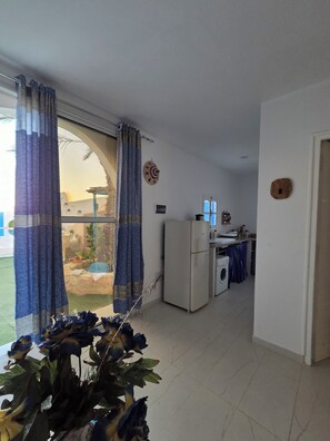 Una habitación con un ventanal grande, un refrigerador, una lavadora y una pequeña cocina.