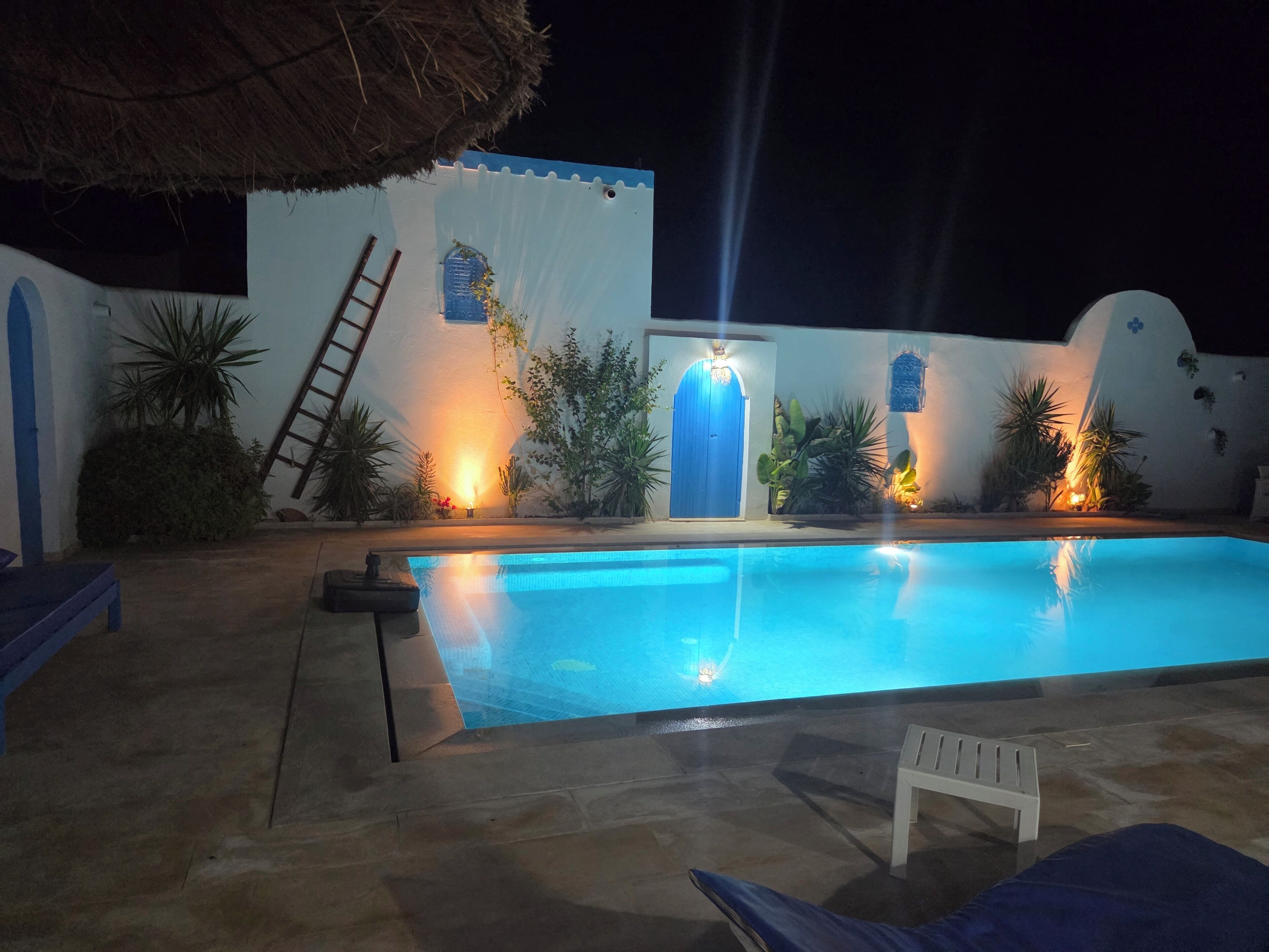 A swimming pool with a blue door, a ladder, and a white chair.