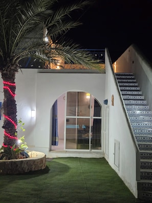A building with a staircase, a glass door entrance, and a palm tree with lights.