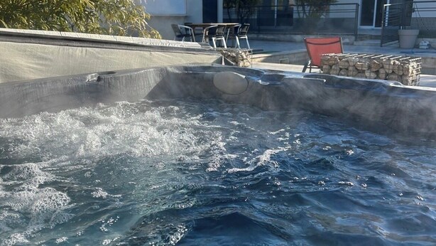 Ein Whirlpool mit fließendem Wasser, umgeben von Gartenmöbeln und einem Gebäude im Hintergrund.