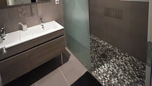 Ein modernes Badezimmer mit Duschkabine aus Glas, einem großen Spiegel und einem Waschtisch mit Becken und zwei Wasserhähnen.
