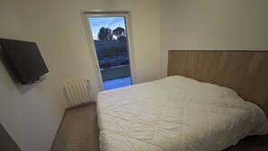 Ein Schlafzimmer mit einem Bett, einem an der Wand befestigten Fernseher und einer Tür zu einem Außenbereich.