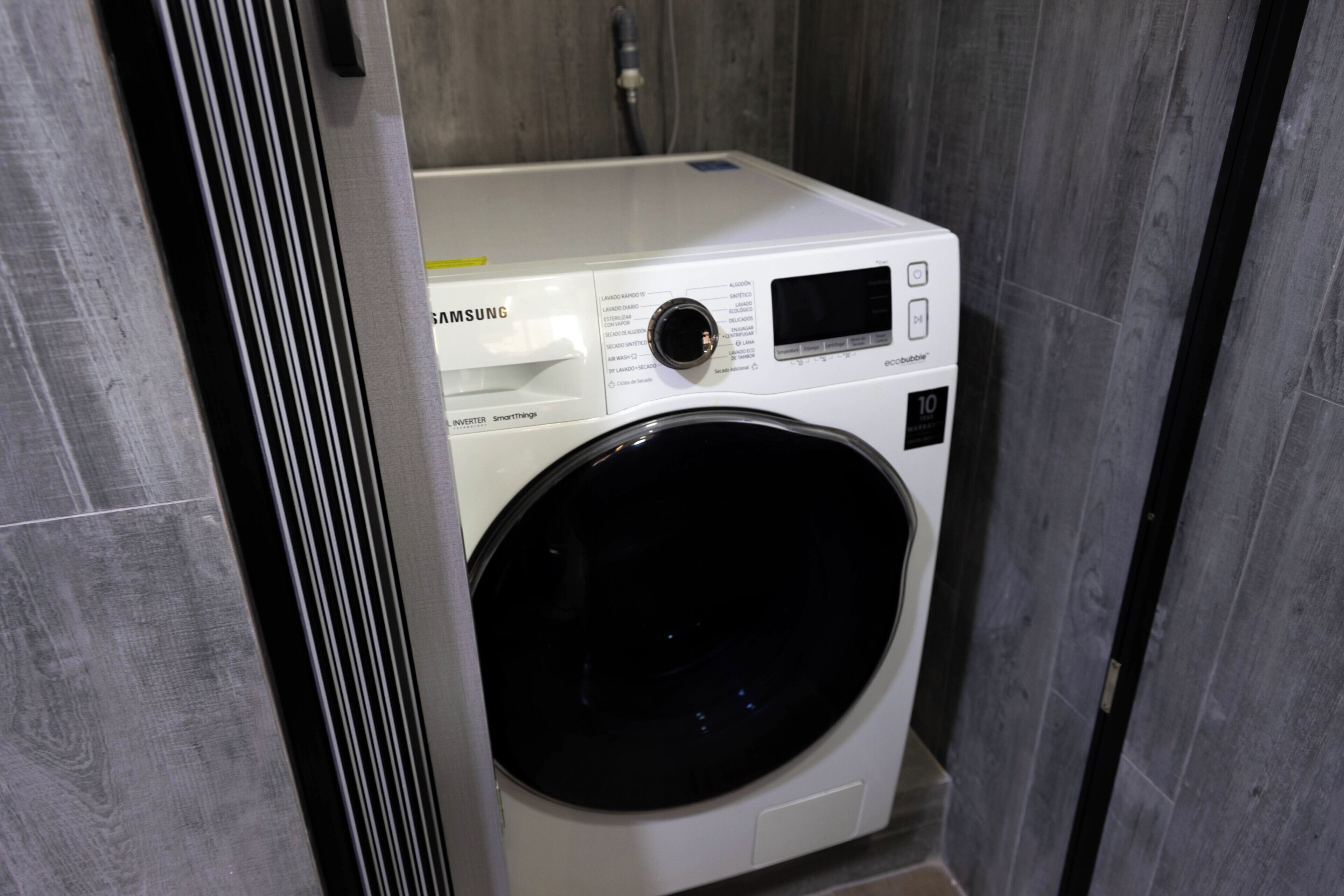 Eine Samsung Smart Inverter Waschmaschine in einem Badezimmer mit grauen Fliesenwänden.