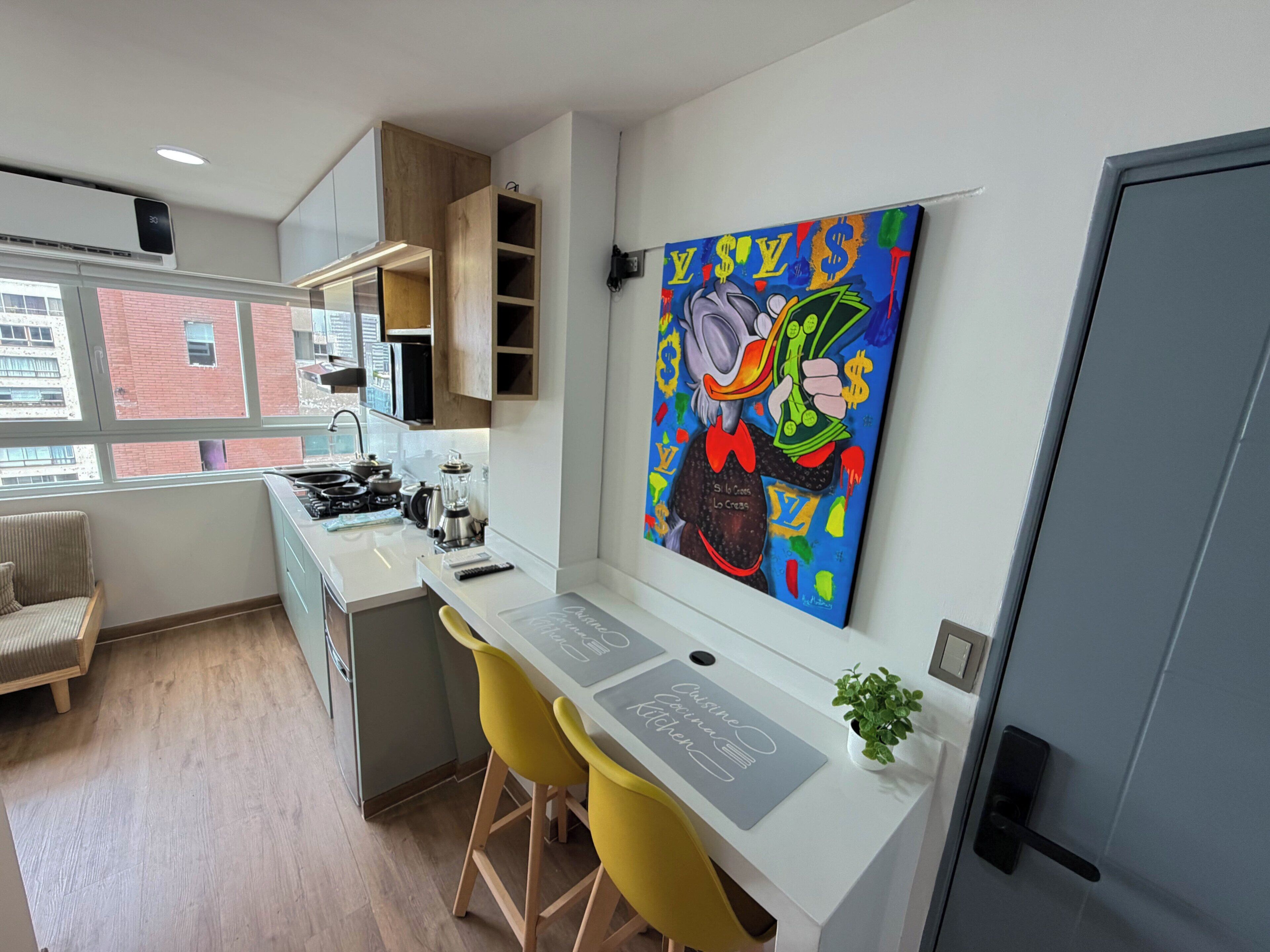 Une cuisine moderne avec un îlot central, des chaises jaunes, un tableau accroché au mur et une vue sur la ville grâce à de grandes fenêtres.