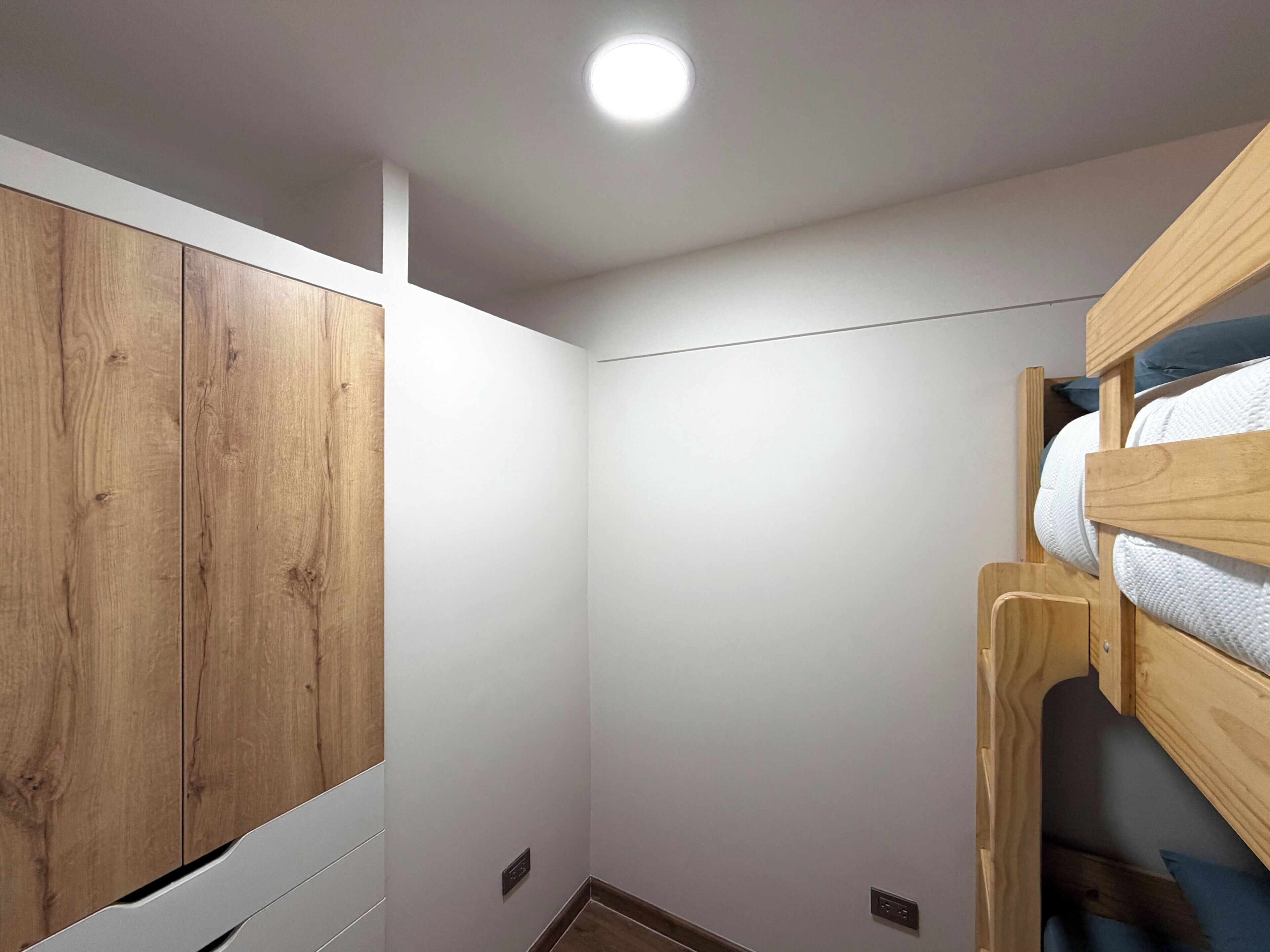 Un letto a castello con struttura in legno e biancheria bianca, un armadio bianco con porta in legno e una luce a incasso nel soffitto.