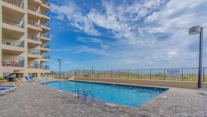 Piscina com salva-vidas de serviço e um deck de tijolos, além de um edifício com varandas.