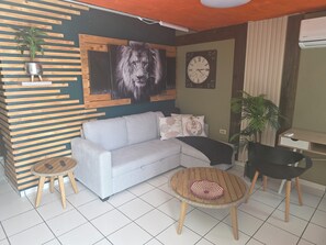 A living room with a sofa, two small round tables, a clock, and a plant. - Bon Homme's / Private space in Cabo Rojo, full equipped / Near Beaches (Cabo Rojo)