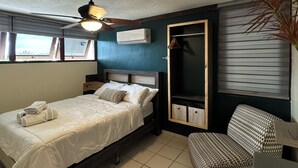 Ein Schlafzimmer mit einem Bett, einem Sessel, einem Deckenventilator, einer Klimaanlage und einem Fenster.