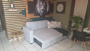 Ein modernes Wohnzimmer mit einem grauen Sofa, einem runden Holztisch, einer Wanduhr und einem Topfpflanzen.