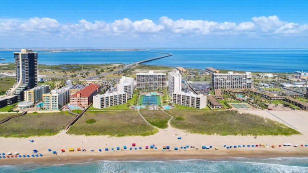 Ein Küstenresort mit mehreren Hotelgebäuden, einem Strand und einer Brücke im Hintergrund.