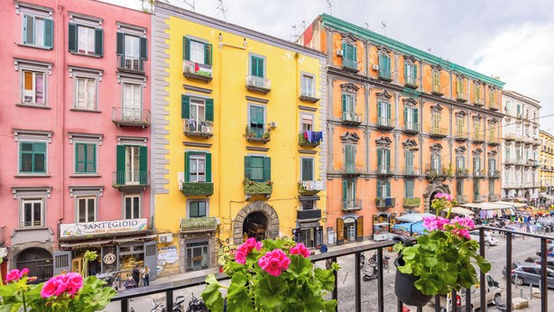 A row of colorful buildings with balconies, a street with parked motorcycles, and a shop with a sign. - BORGO VERGINI SUITES (Naples)