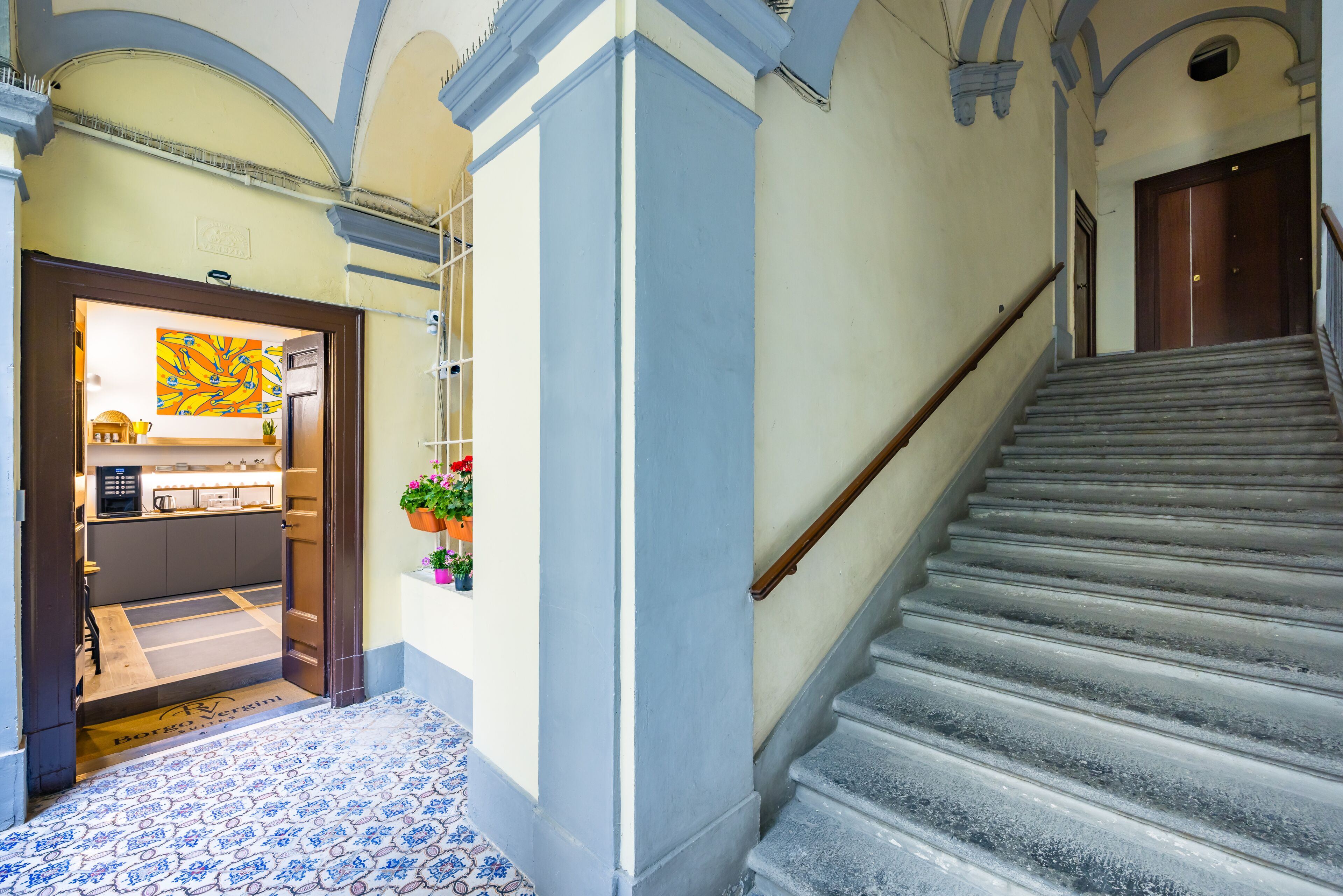 A hotel hallway with a staircase, a kitchen area, and a decorative painting.