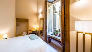 A hotel room with a bed, a desk, a mirror, a window with a view, and a balcony with flowers. - BORGO VERGINI SUITES (Naples)