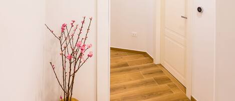 Un couloir avec un plancher en bois, une porte blanche et un vase rempli de fleurs roses.