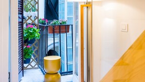 A narrow hallway with a modern lamp, a wooden door, and a view of a balcony with potted plants. - BORGO VERGINI SUITES (Naples)