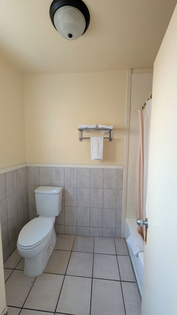 A bathroom with a toilet, a towel rack, and a shower area. - Cloud 9 Motel Cypress Buena Park (Cypress)