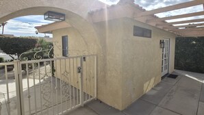 Un espacio al aire libre cubierto, con piso de concreto, una reja metálica y un ventanal pequeño.