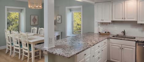 A kitchen with white cabinets, a granite countertop, and a dining area with white chairs.