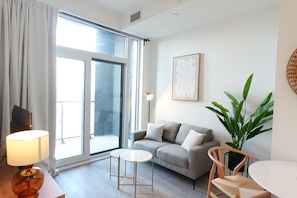 A modern living room with a sofa, a small round table, a lamp, a potted plant, and a large window.