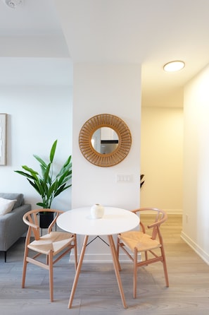 A dining area with a round table, two chairs, a potted plant, a wall-mounted mirror, and a light fixture.