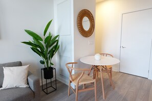 Une pièce avec un canapé gris, une plante en pot, une table ronde avec des chaises et un miroir en bois accroché au mur.