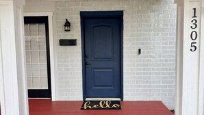 Een blauwe deur met een 'hello'-mat, een witte bakstenen muur en een brievenbus.