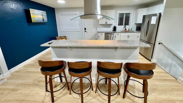 Een moderne keuken met een centraal eiland, barstoelen, een roestvrijstalen koelkast en een schilderij aan de muur.