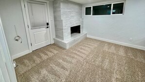 Een kamer met een open haard, vloerbedekking, witte muren en een deur met een raam.