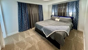 Een slaapkamer met een bed, gordijnen, een plafondlamp en een vloerbedekking.