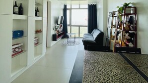 A modern living room with a sofa, a dining table with a patterned runner, and built-in shelving with various items. - Modern City Escape at Forbeswood Parklane (Taguig City)