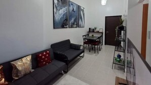 A living room with a sofa, a dining table with chairs, and a staircase leading to another level. - Prime Living at Forbeswood Parklane (Taguig City)