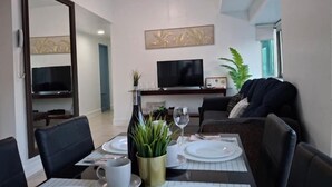 A dining area with a table set for two, a television above the table, and a sofa in the background. - Comfort & Convenience at Forbeswood Parklane (Taguig City)