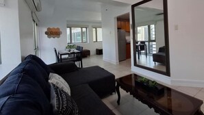 A modern living room with a large mirror, a sofa, a dining table with chairs, and a kitchen area visible through an open doorway. - Comfort & Convenience at Forbeswood Parklane (Taguig City)
