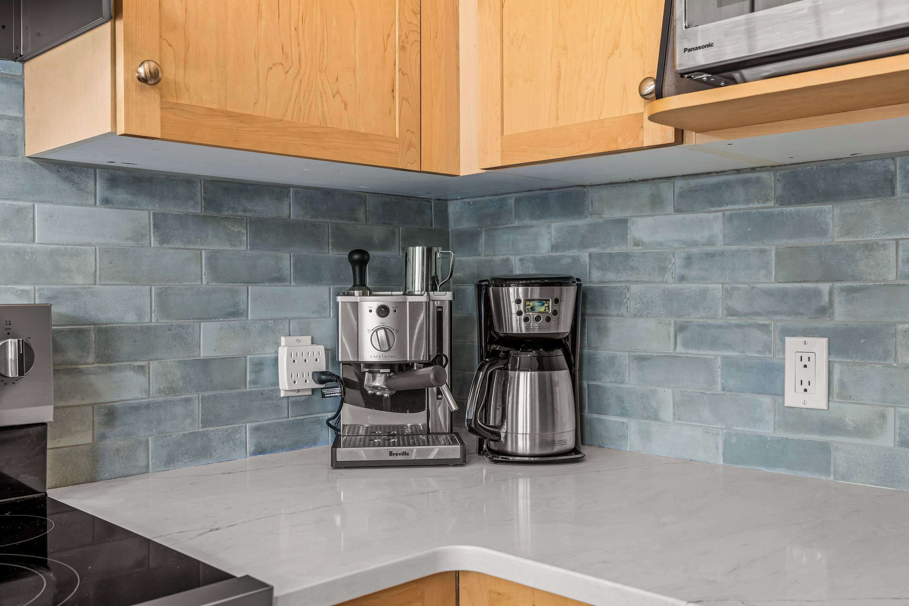 Une cuisine équipée d’une machine à expresso Breville, d’un four à micro-ondes Panasonic et d’une machine à café, le tout posé sur un plan de travail blanc.